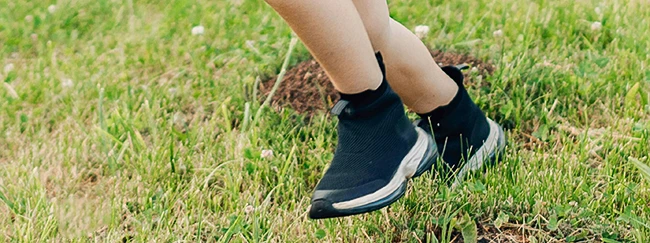 Das Symbolbild zeigt die Detailaufnahme von Kindersportschuhen, die über eine Wiese rennen. Es ist Teil der Seite des Schuheinlagen Herstellers Mergel und Sohn aus Langenfeld und Ludwigshafen. Dieser fertigt auch Einlagen für Kinderschuhe.